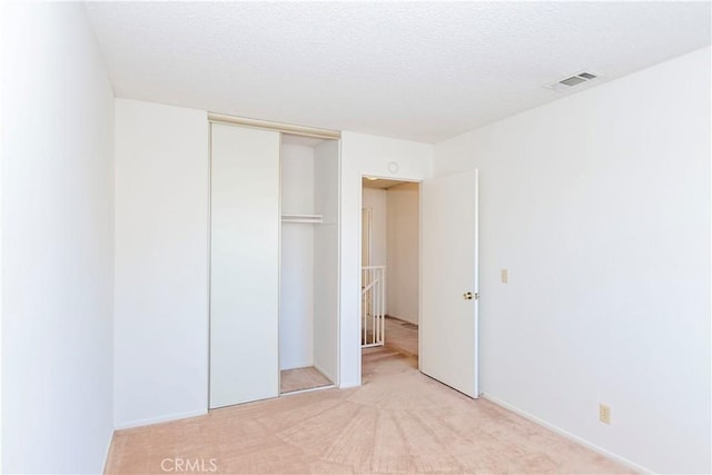 unfurnished bedroom with a closet, visible vents, a textured ceiling, and light carpet