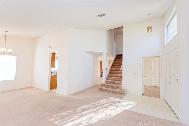 unfurnished living room featuring visible vents, a high ceiling, carpet, a chandelier, and stairs