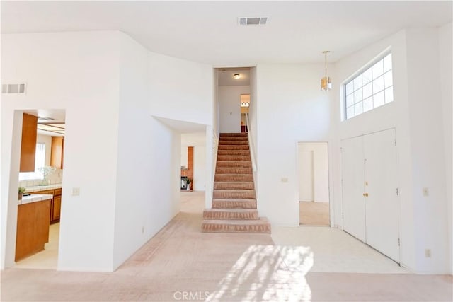 entryway featuring stairway, light colored carpet, visible vents, and a towering ceiling