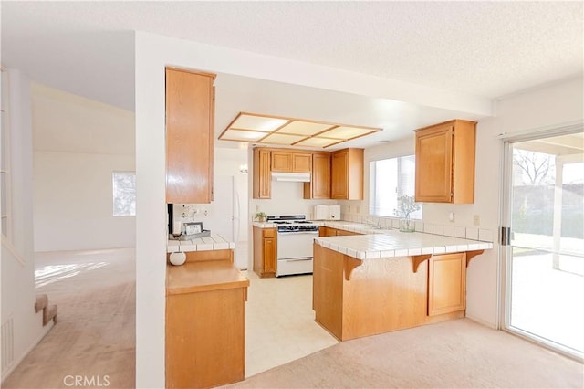 kitchen featuring tile counters, light floors, white gas range oven, a peninsula, and a kitchen breakfast bar