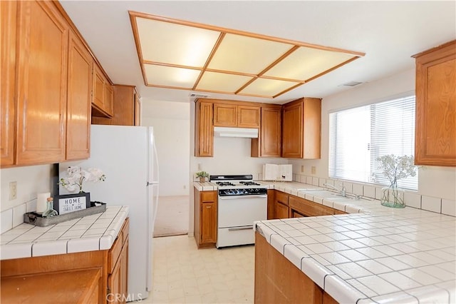 kitchen featuring visible vents, tile counters, under cabinet range hood, light floors, and white appliances