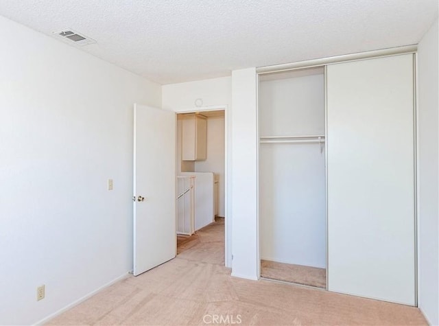 unfurnished bedroom featuring a closet, visible vents, light colored carpet, and a textured ceiling