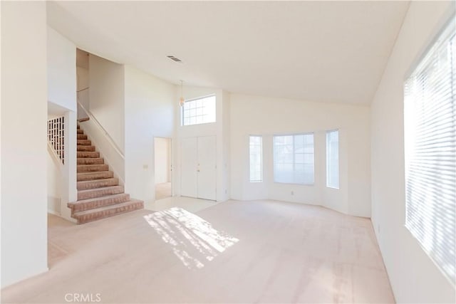 carpeted entrance foyer with stairway, visible vents, and high vaulted ceiling