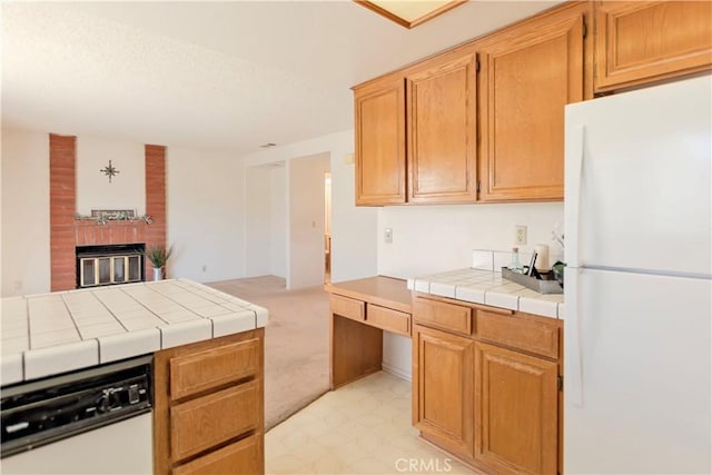 kitchen featuring a brick fireplace, tile counters, light floors, dishwashing machine, and freestanding refrigerator