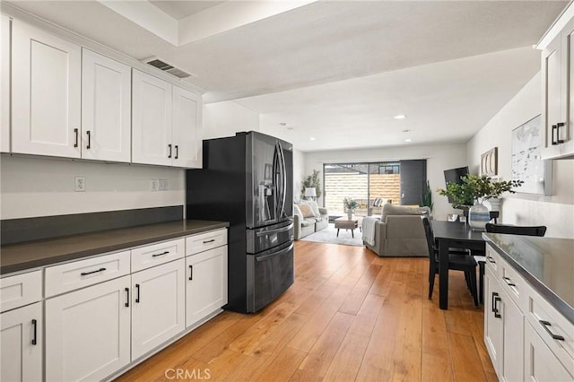 kitchen with visible vents, light wood-style flooring, white cabinets, dark countertops, and fridge with ice dispenser