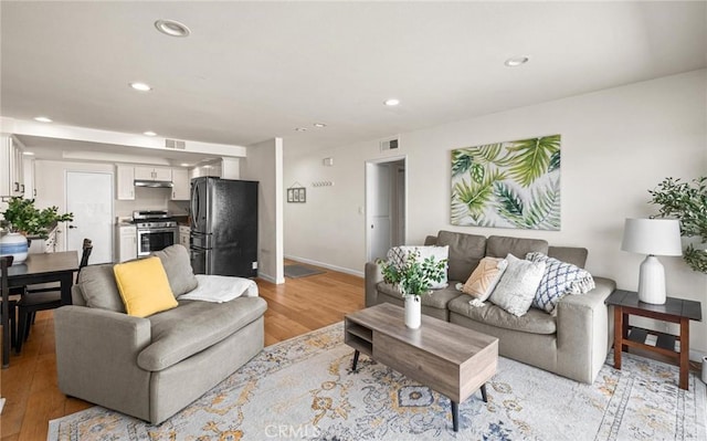 living room featuring light wood finished floors, visible vents, recessed lighting, and baseboards