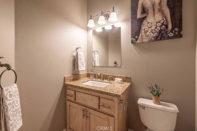 bathroom with vanity, toilet, and a textured wall