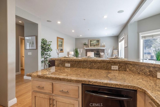 kitchen featuring light wood finished floors, black dishwasher, light stone counters, recessed lighting, and a fireplace