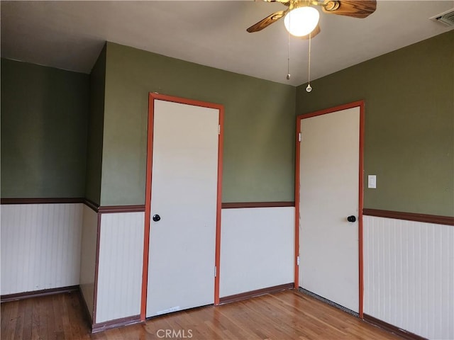 spare room with a ceiling fan, visible vents, wood finished floors, and a wainscoted wall