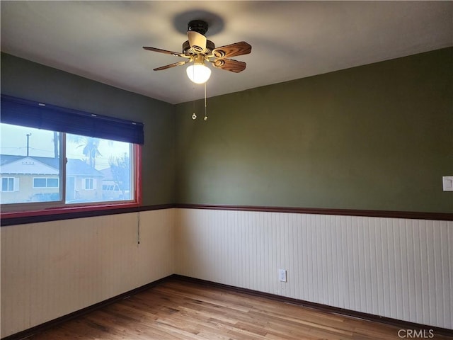 empty room with a ceiling fan, wood finished floors, and a wainscoted wall