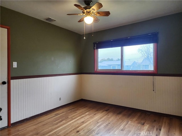 empty room featuring ceiling fan, wood finished floors, visible vents, and wainscoting