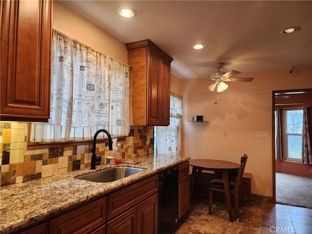 kitchen featuring ceiling fan, light stone countertops, black dishwasher, decorative backsplash, and a sink