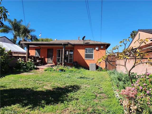 back of house with stucco siding, a lawn, and central AC unit