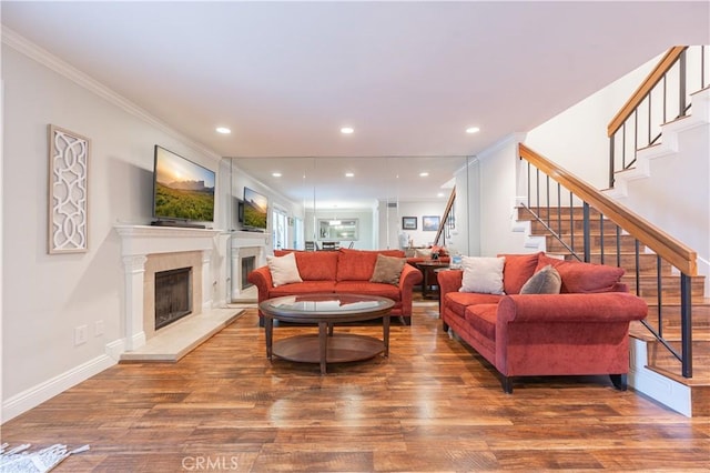 living room with a fireplace with raised hearth, ornamental molding, wood finished floors, recessed lighting, and stairway