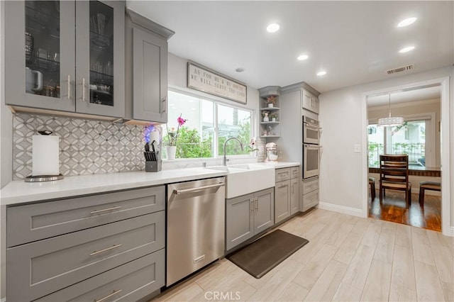 kitchen featuring light wood finished floors, visible vents, gray cabinets, stainless steel appliances, and a sink