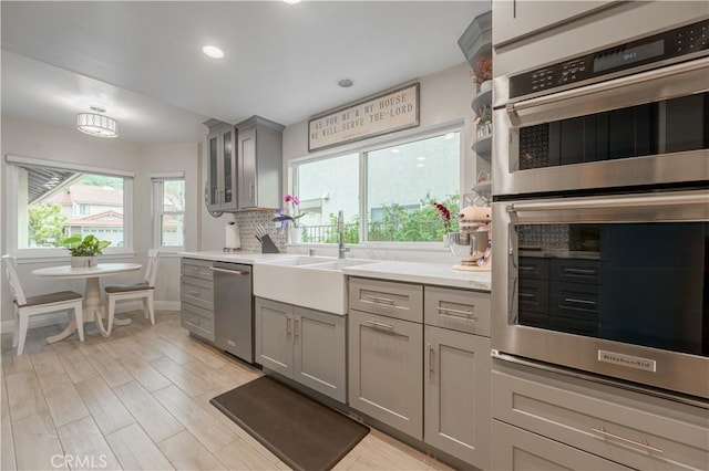 kitchen featuring backsplash, light countertops, gray cabinets, stainless steel appliances, and a sink