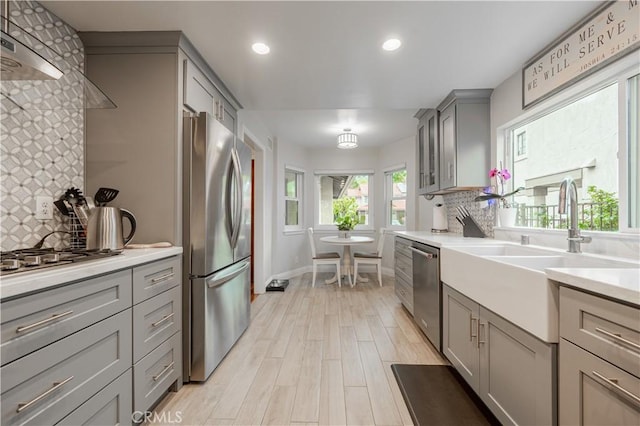 kitchen featuring a sink, gray cabinetry, light countertops, stainless steel appliances, and backsplash