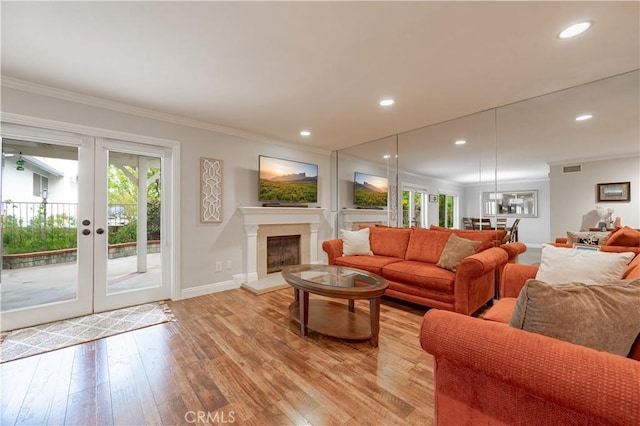 living area featuring light wood finished floors, a fireplace with raised hearth, french doors, and ornamental molding