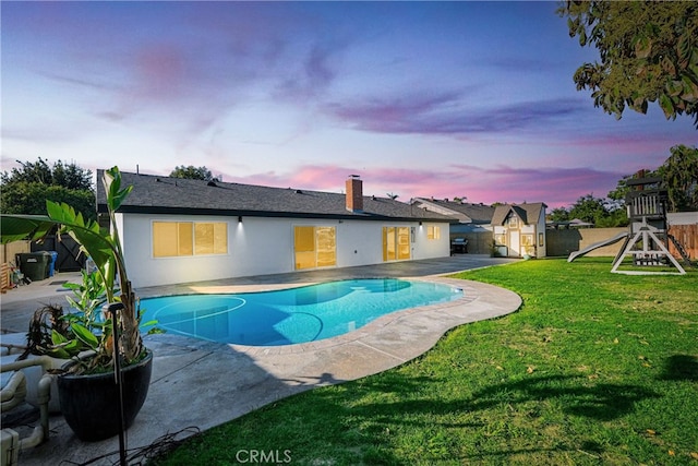 pool at dusk featuring an outdoor structure, a patio area, a storage shed, a playground, and a lawn