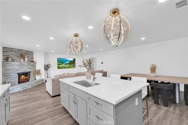 kitchen with visible vents, light wood finished floors, an island with sink, a fireplace, and a sink