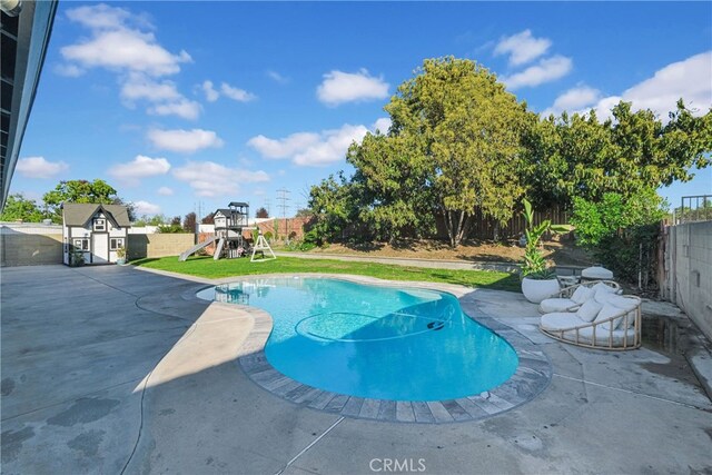 view of swimming pool with a fenced backyard, an outdoor structure, a storage unit, a playground, and a patio area