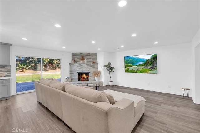 living room featuring recessed lighting, baseboards, a stone fireplace, and light wood finished floors