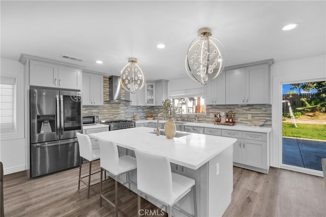 kitchen with a notable chandelier, wall chimney exhaust hood, visible vents, and stainless steel fridge with ice dispenser