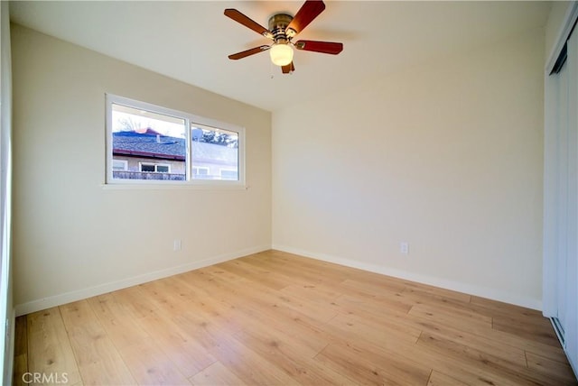 spare room featuring light wood-style flooring, a ceiling fan, and baseboards