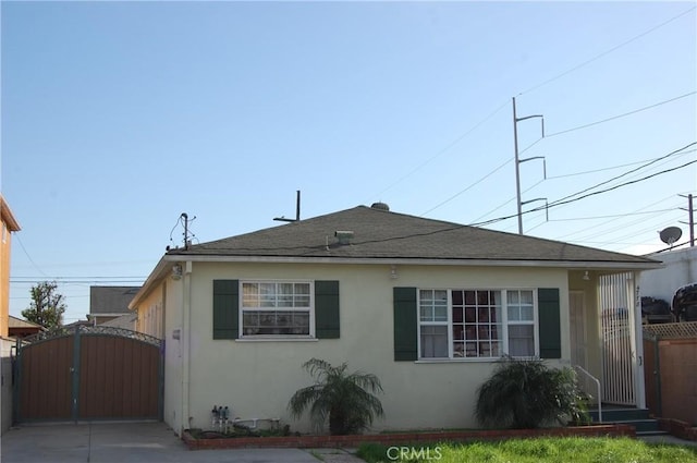 view of front facade featuring stucco siding, fence, roof with shingles, and a gate