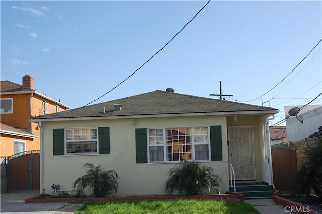 bungalow featuring stucco siding, roof with shingles, and a gate