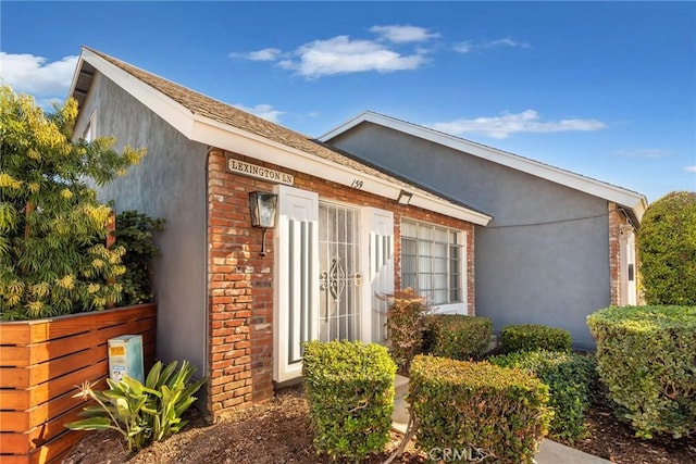 view of property exterior featuring brick siding, stucco siding, and fence