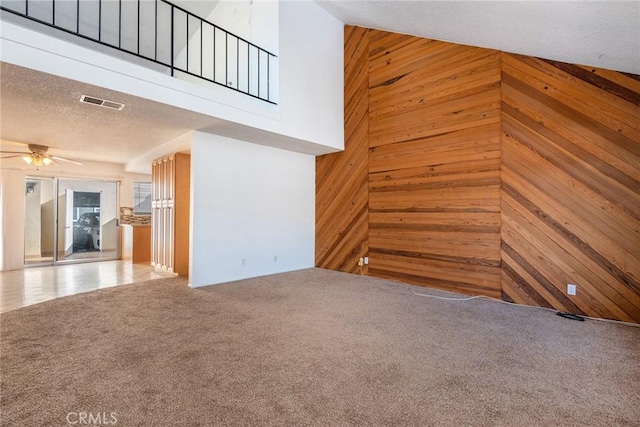 unfurnished living room featuring a high ceiling, ceiling fan, carpet floors, wood walls, and visible vents