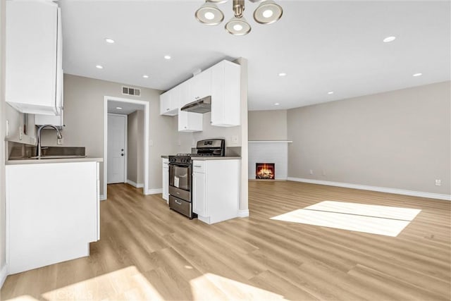 kitchen featuring visible vents, under cabinet range hood, gas stove, a fireplace, and light wood finished floors