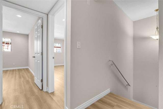 corridor featuring light wood-type flooring, an upstairs landing, and baseboards