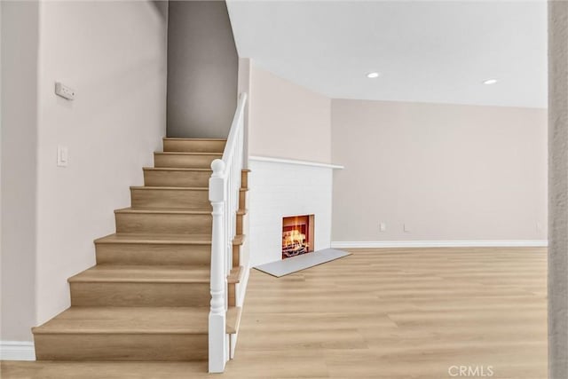 stairs featuring recessed lighting, baseboards, a brick fireplace, and wood finished floors