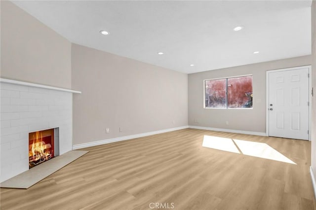 unfurnished living room with recessed lighting, baseboards, a brick fireplace, and light wood-style flooring