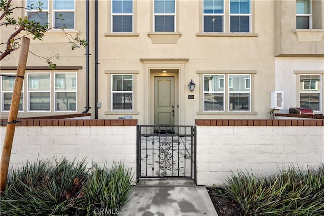 doorway to property with a gate, fence, and stucco siding