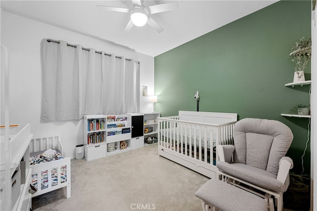 carpeted bedroom featuring a crib and a ceiling fan