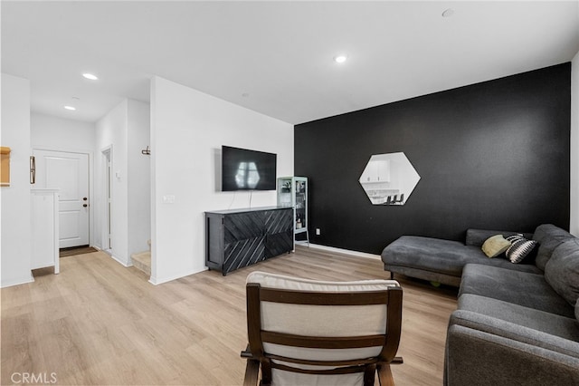 living room with an accent wall, recessed lighting, light wood-type flooring, and baseboards