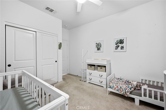 carpeted bedroom with a closet, visible vents, a crib, and ceiling fan