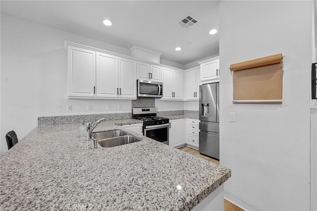 kitchen featuring visible vents, a peninsula, a sink, stainless steel appliances, and white cabinetry