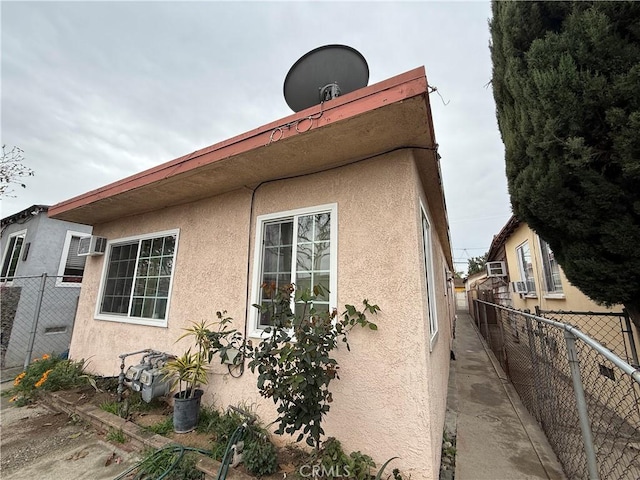 view of home's exterior with stucco siding, a wall mounted AC, and fence