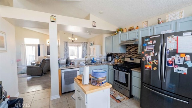 kitchen with under cabinet range hood, a sink, stainless steel appliances, light tile patterned floors, and lofted ceiling