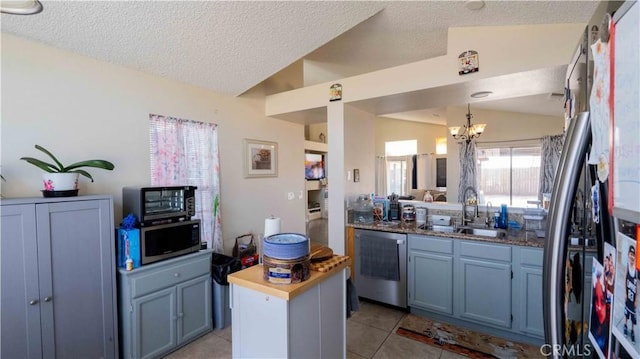 kitchen with stainless steel microwave, lofted ceiling, dishwashing machine, light tile patterned flooring, and a sink