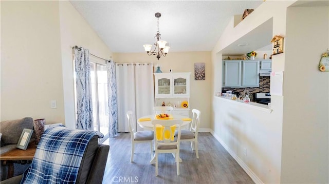 dining room featuring a chandelier, baseboards, wood finished floors, and vaulted ceiling