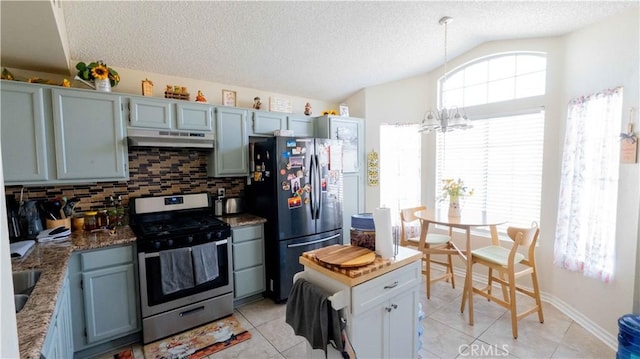 kitchen with under cabinet range hood, stainless steel appliances, decorative backsplash, lofted ceiling, and a chandelier