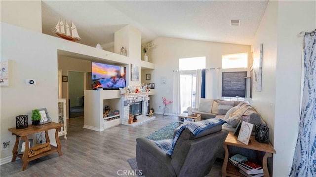 living area featuring a glass covered fireplace, high vaulted ceiling, visible vents, and wood finished floors