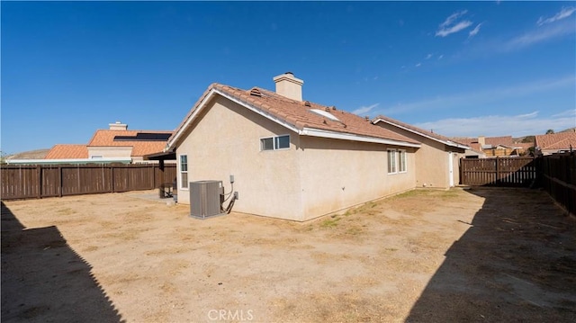 rear view of house with stucco siding, central AC, a fenced backyard, and a chimney