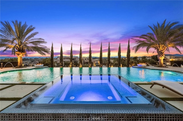 pool at dusk with a patio area, an in ground hot tub, and an infinity pool