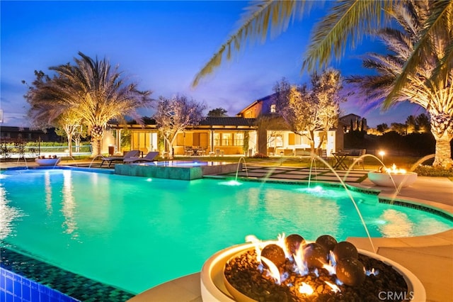 pool at dusk featuring a patio, a fire pit, and a pool with connected hot tub